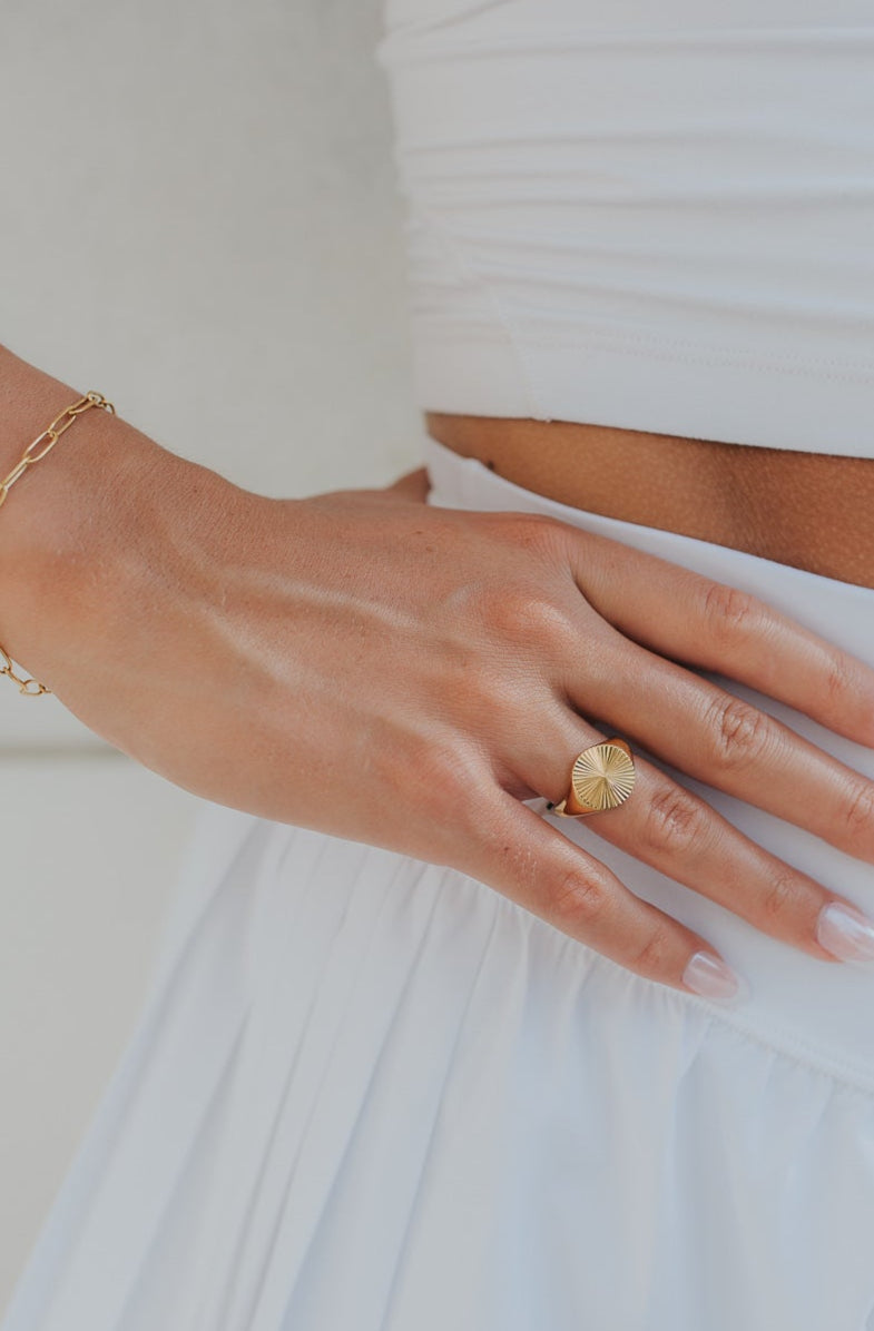 Person wearing a white outfit with a gold ring and bracelet on a neutral background